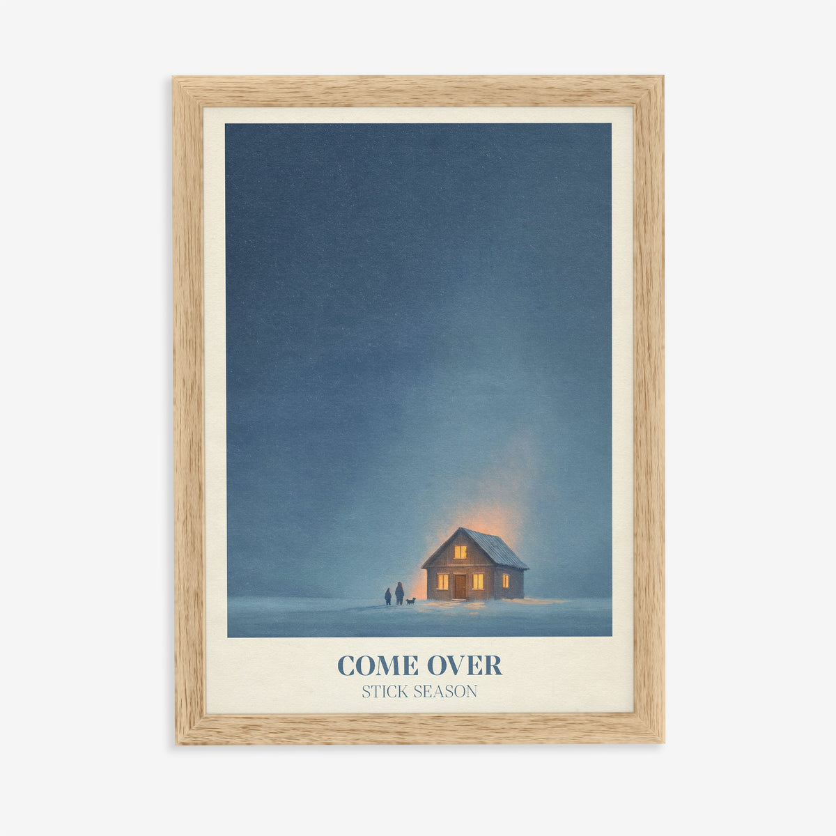Come Over Noah Kahan print of a warm glowing cabin under a deep blue winter sky, in an oak frame on a plain wall
