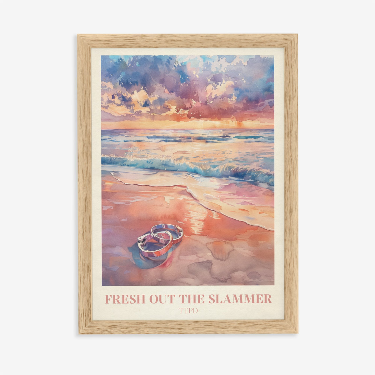Fresh Out The Slammer Taylor Swift print of open handcuffs on wet sand at a pink sunset, in an oak frame on a plain wall