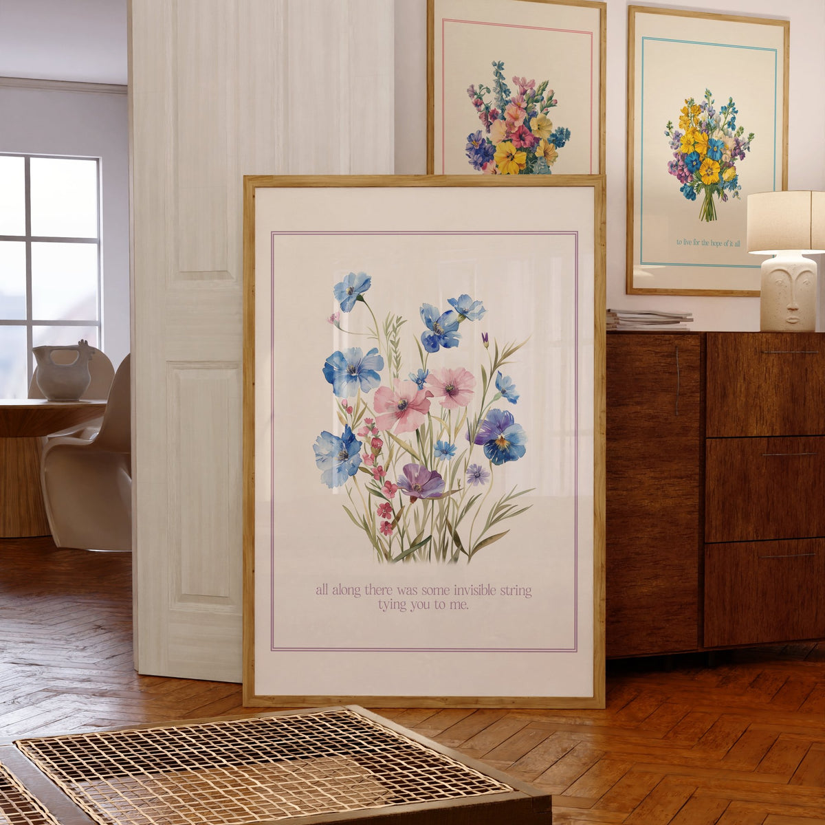 Invisible String Botanical Taylor Swift print of blue and pink wildflowers, framed, leaning against a chest of drawers