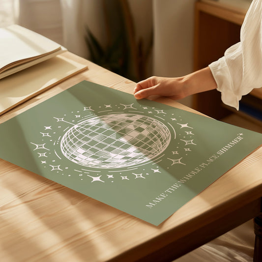 Mirrorball Taylor Swift print of a white line-drawn disco ball on sage green, laid flat on a sunny table
