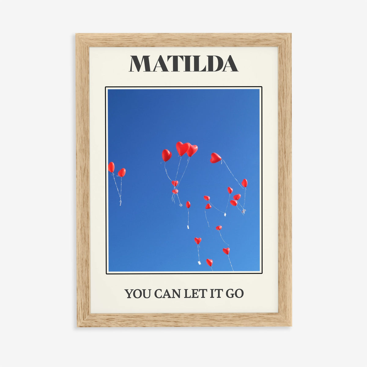 Matilda Harry Styles print of red heart balloons in a deep blue sky, in an oak frame on a plain wall