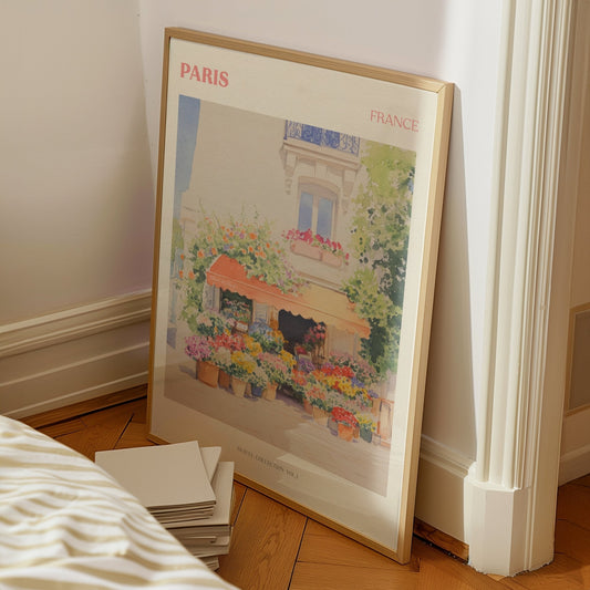 Paris travel print of a flower stall with an orange awning and pots of bright flowers, framed, leaning by a bed