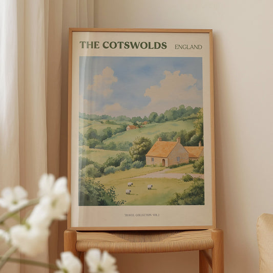 Cotswolds travel print of a honey-coloured stone cottage in rolling green hills with sheep, on a wooden chair