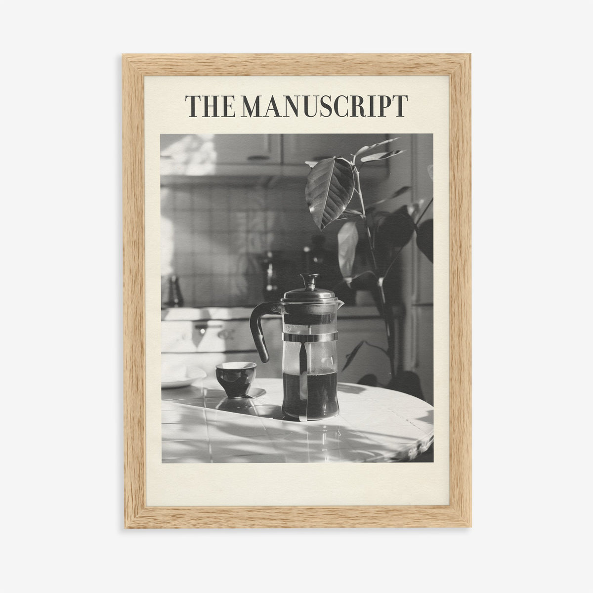 The Manuscript Taylor Swift print of a black and white French press and cup on a sunlit table, in an oak frame on a plain wall