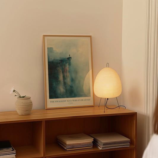 The Smallest Man Who Ever Lived Taylor Swift print of a lone figure on a misty blue cliff, framed on a shelf beside a paper lantern
