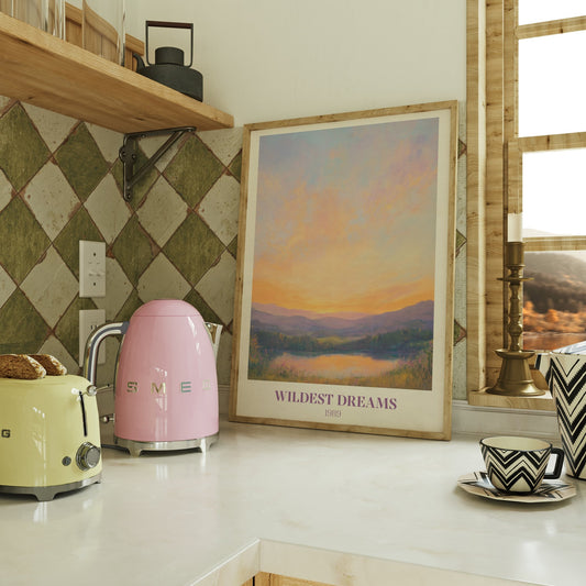 Wildest Dreams Taylor Swift print of a painted peach and lilac sunset over hills and a lake, framed on a kitchen counter