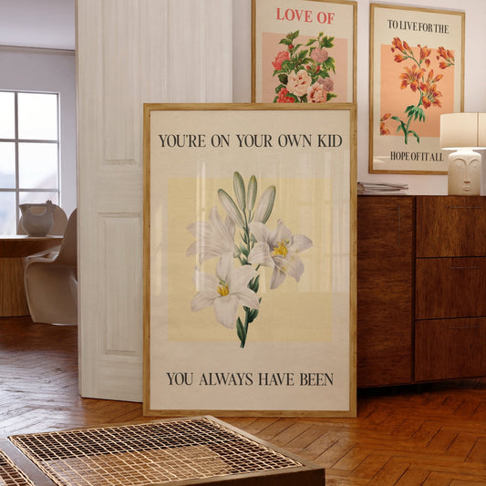 You’re On Your Own Kid Botanical Taylor Swift lyric print of white lilies on yellow, framed beside other New York prints
