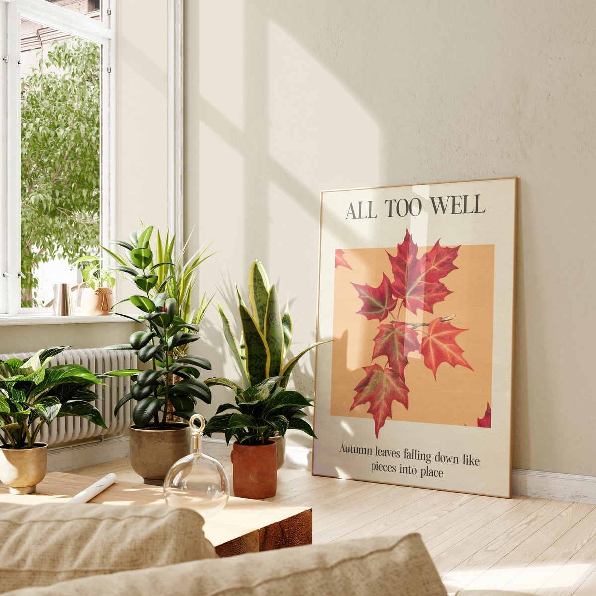 All Too Well Leaf Taylor Swift print of red maple leaves on a peach square, framed, leaning against a wall beside potted plants