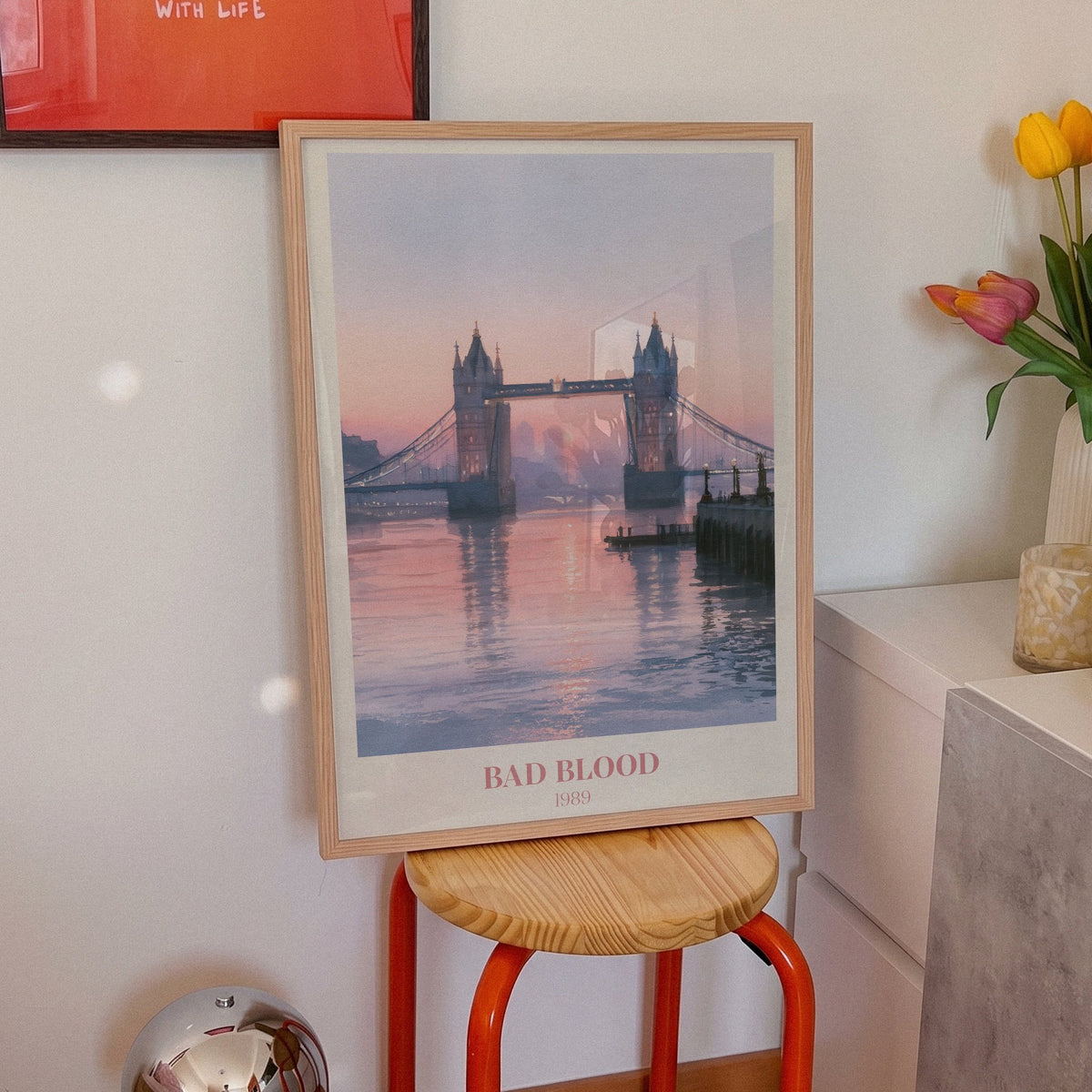 Bad Blood Taylor Swift print of Tower Bridge at a pink sunset, on an orange stool beside tulips
