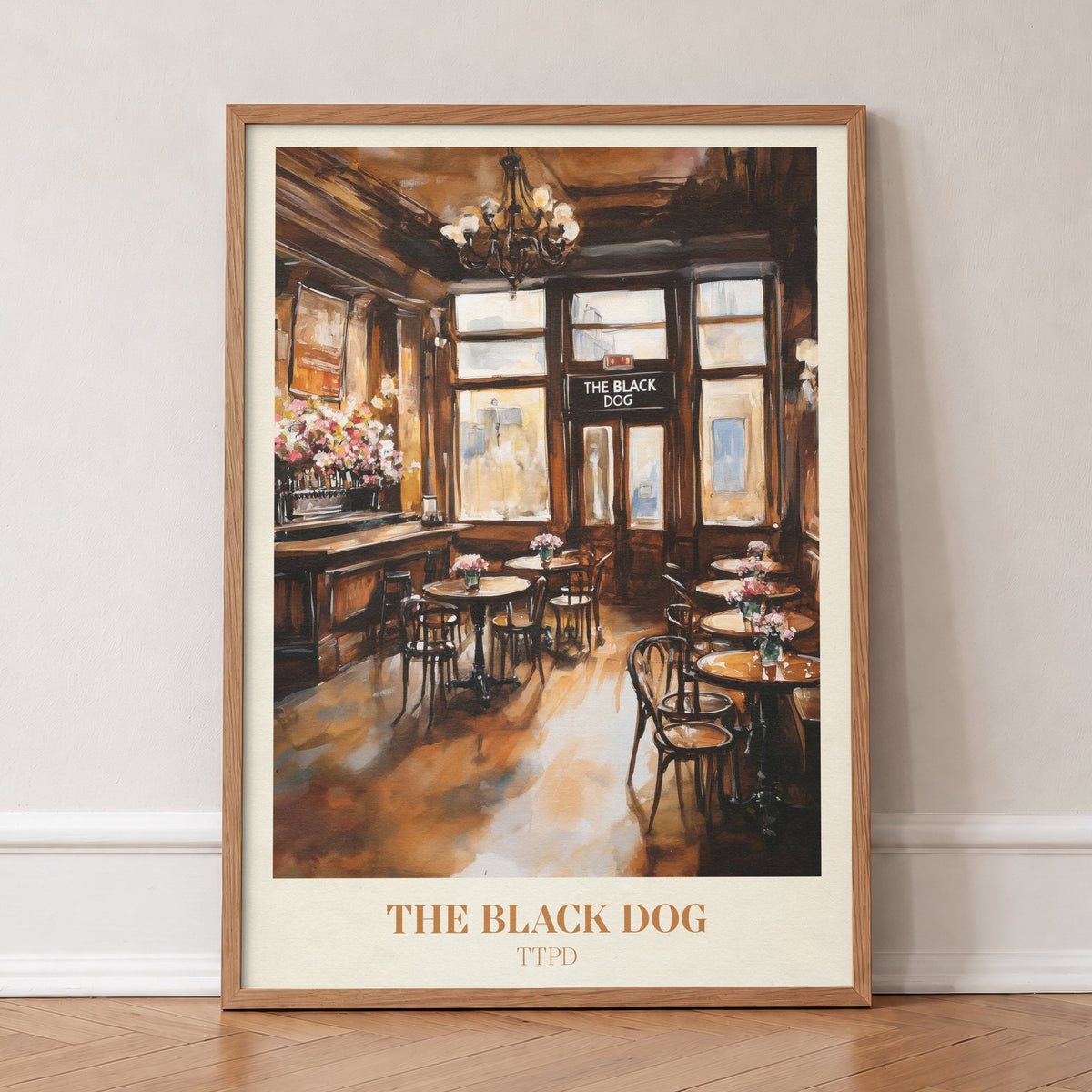 The Black Dog Taylor Swift print of a wood-panelled pub with bistro tables and a chandelier, in an oak frame, leaning against a wall on a herringbone floor