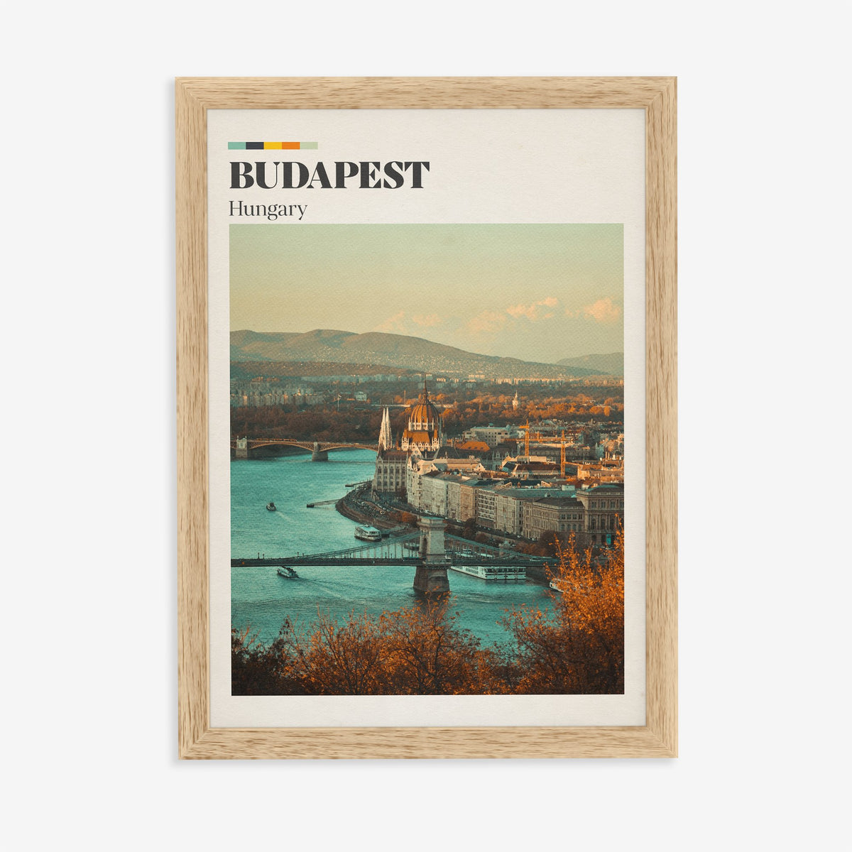 Budapest travel print of the Parliament dome above the Danube, framed by autumn trees, in an oak frame on a plain wall