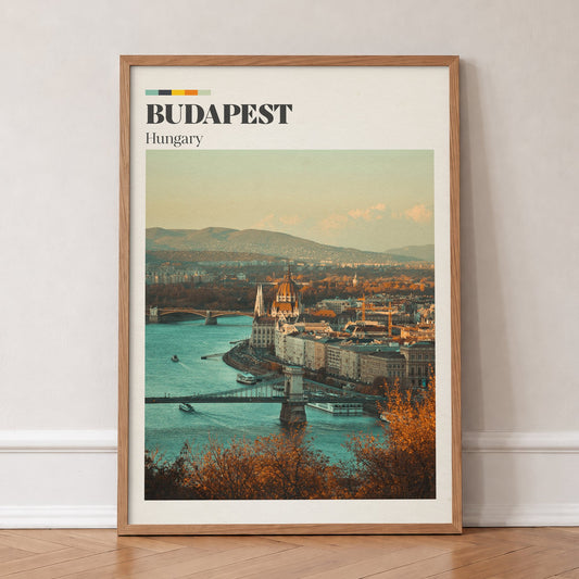 Budapest travel print of the Parliament dome above the Danube, framed by autumn trees, in an oak frame, leaning against a wall on a herringbone floor