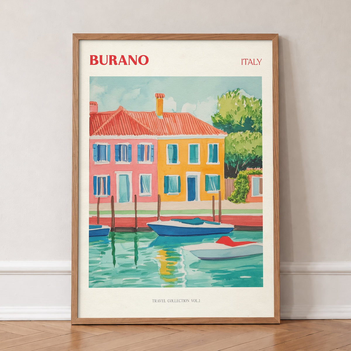 Burano travel print of brightly painted red, orange and yellow houses with boats on a canal, in an oak frame, leaning against a wall on a herringbone floor