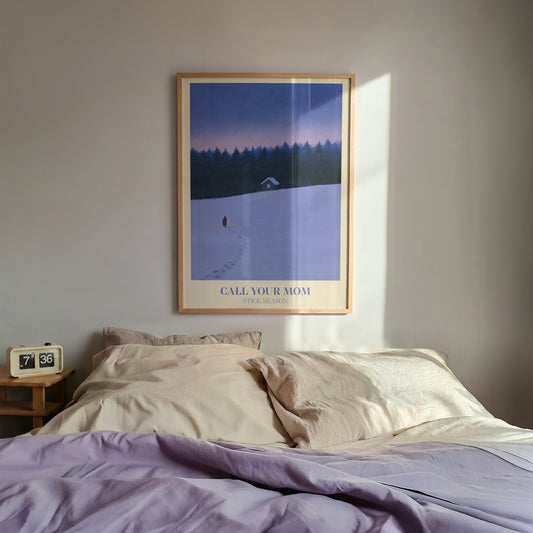 Call Your Mom Winter Noah Kahan print of a lone walker heading to a lit cabin in the snow, hung above a bed with lilac bedding