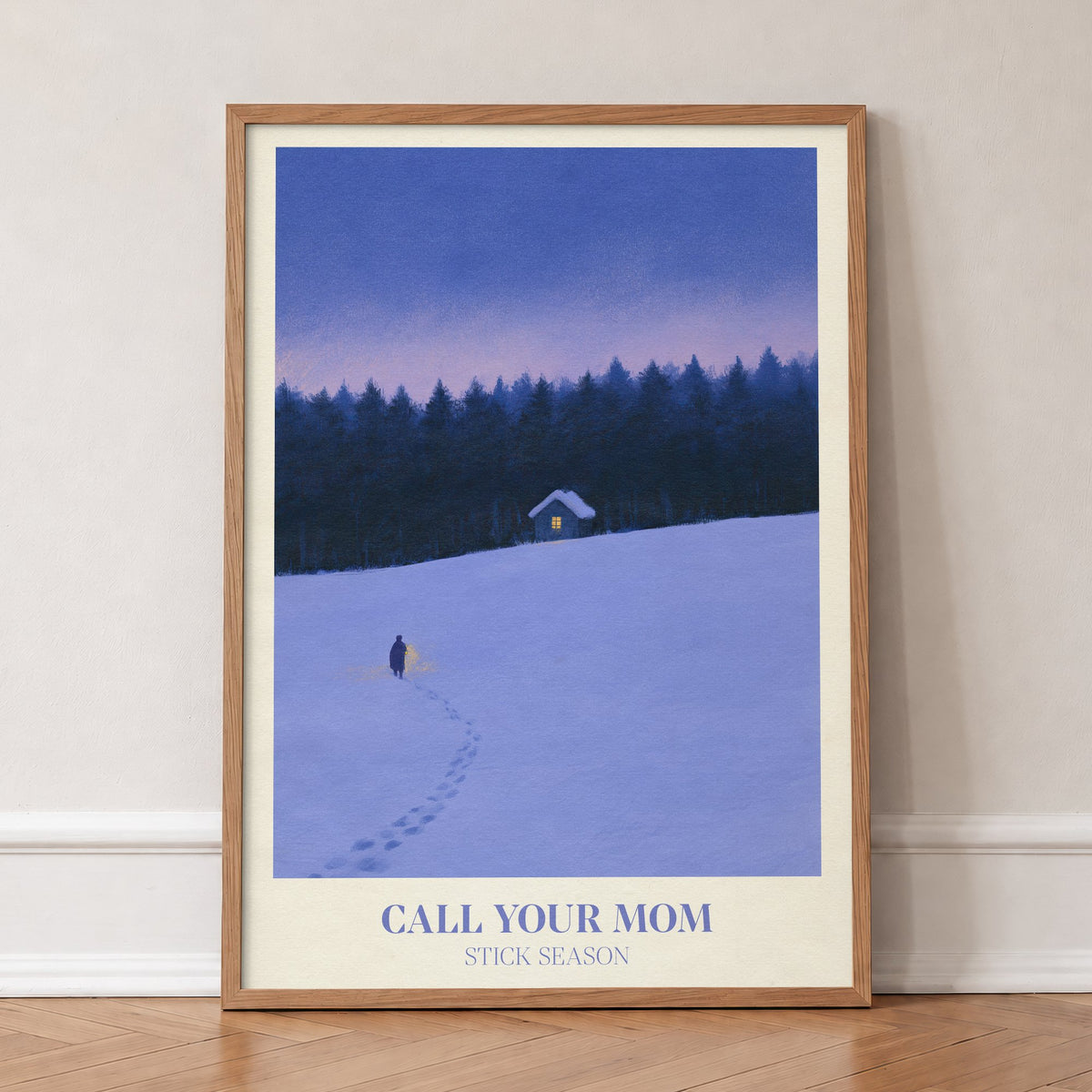 Call Your Mom Winter Noah Kahan print of a lone walker heading to a lit cabin in the snow, in an oak frame, leaning against a wall