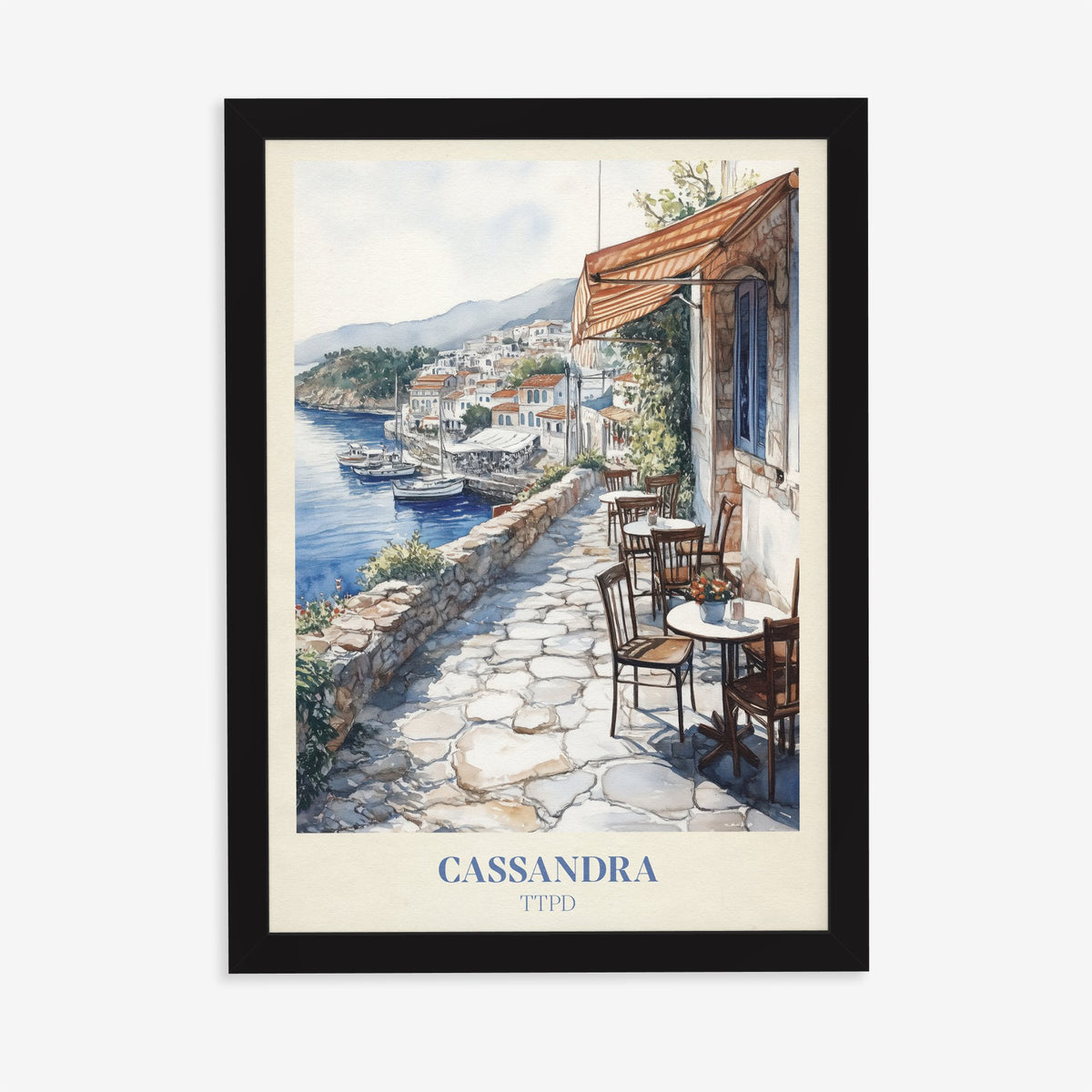 Cassandra Taylor Swift print of a cobbled café terrace above a whitewashed harbour town, in a black frame on a plain wall