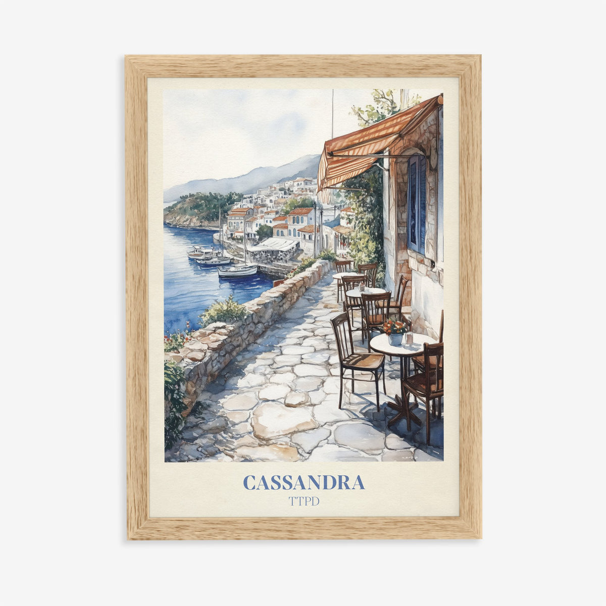 Cassandra Taylor Swift print of a cobbled café terrace above a whitewashed harbour town, in an oak frame on a plain wall