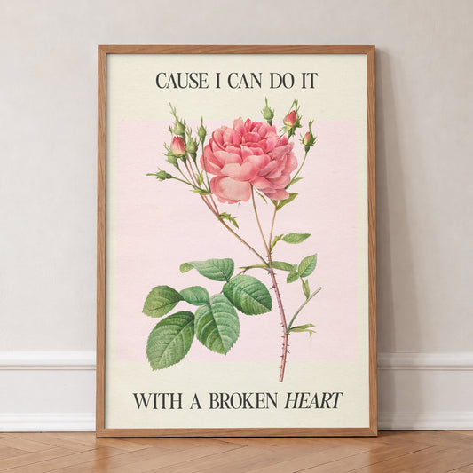 Cause I Can Do It With A Broken Heart Taylor Swift print of a coral pink rose on pale pink, in an oak frame, leaning against a wall on a herringbone floor