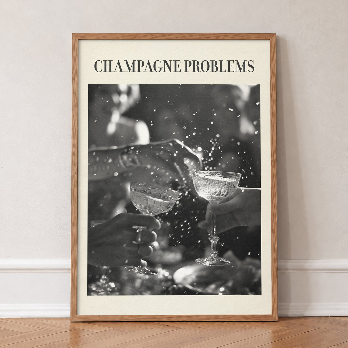 Champagne Problems Retro Taylor Swift print of two champagne coupes clinking in black and white, in an oak frame, leaning against a wall on a herringbone floor