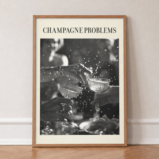 Champagne Problems Retro Taylor Swift print of two champagne coupes clinking in black and white, in an oak frame, leaning against a wall on a herringbone floor