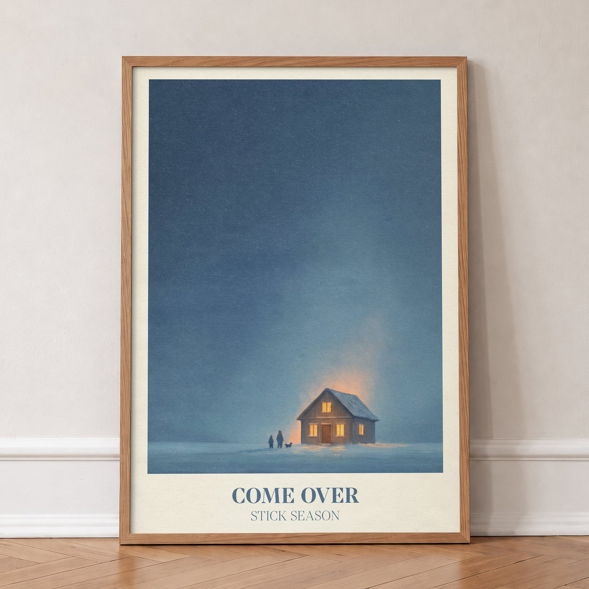 Come Over Noah Kahan print of a warm glowing cabin under a deep blue winter sky, in an oak frame, leaning against a wall on a herringbone floor