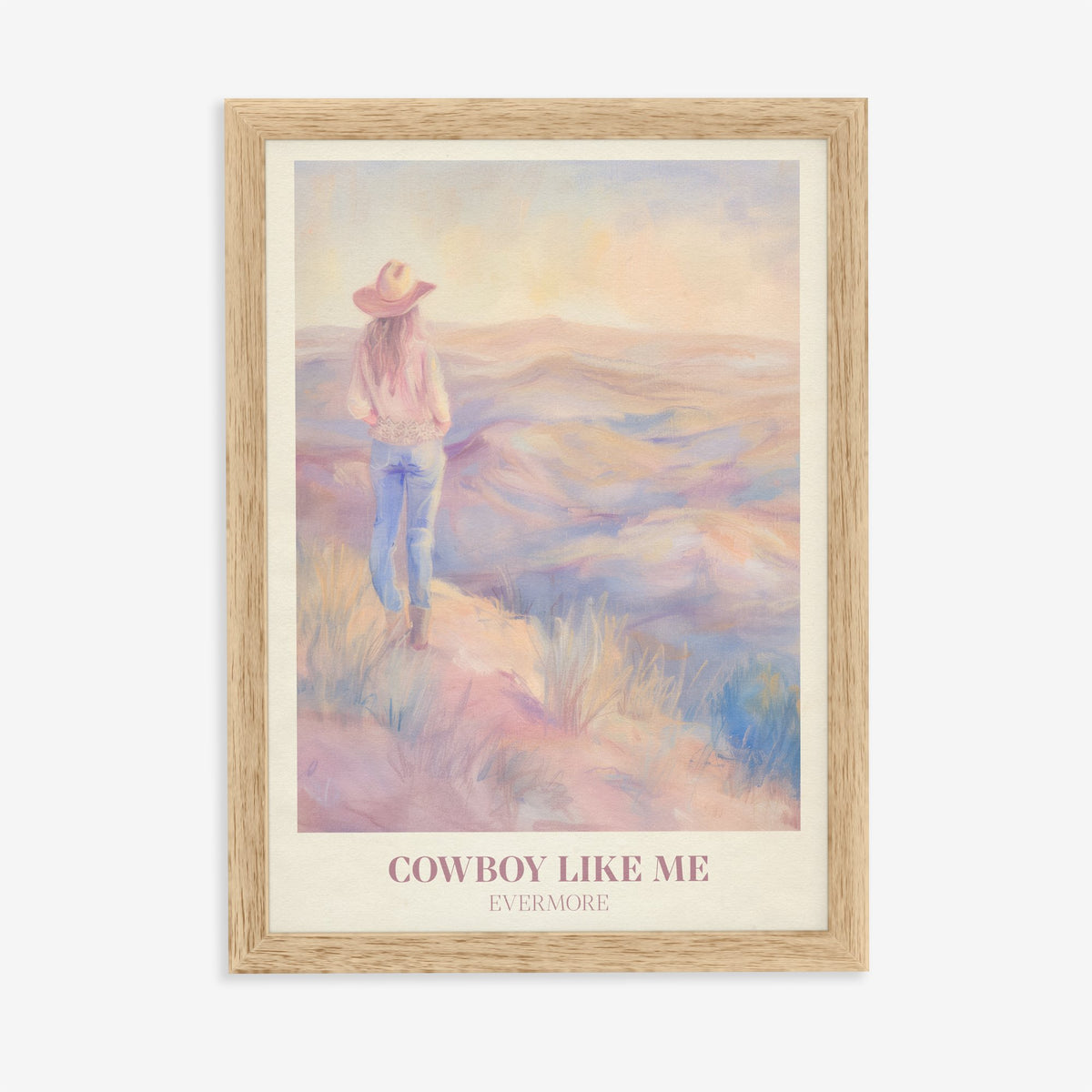 Cowboy Like Me Taylor Swift print of a cowgirl looking out over pastel hills at sunset, in an oak frame on a plain wall