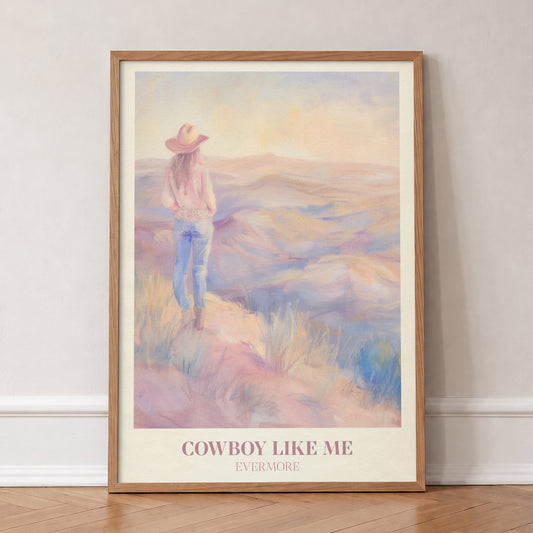 Cowboy Like Me Taylor Swift print of a cowgirl looking out over pastel hills at sunset, in an oak frame, leaning against a wall on a herringbone floor