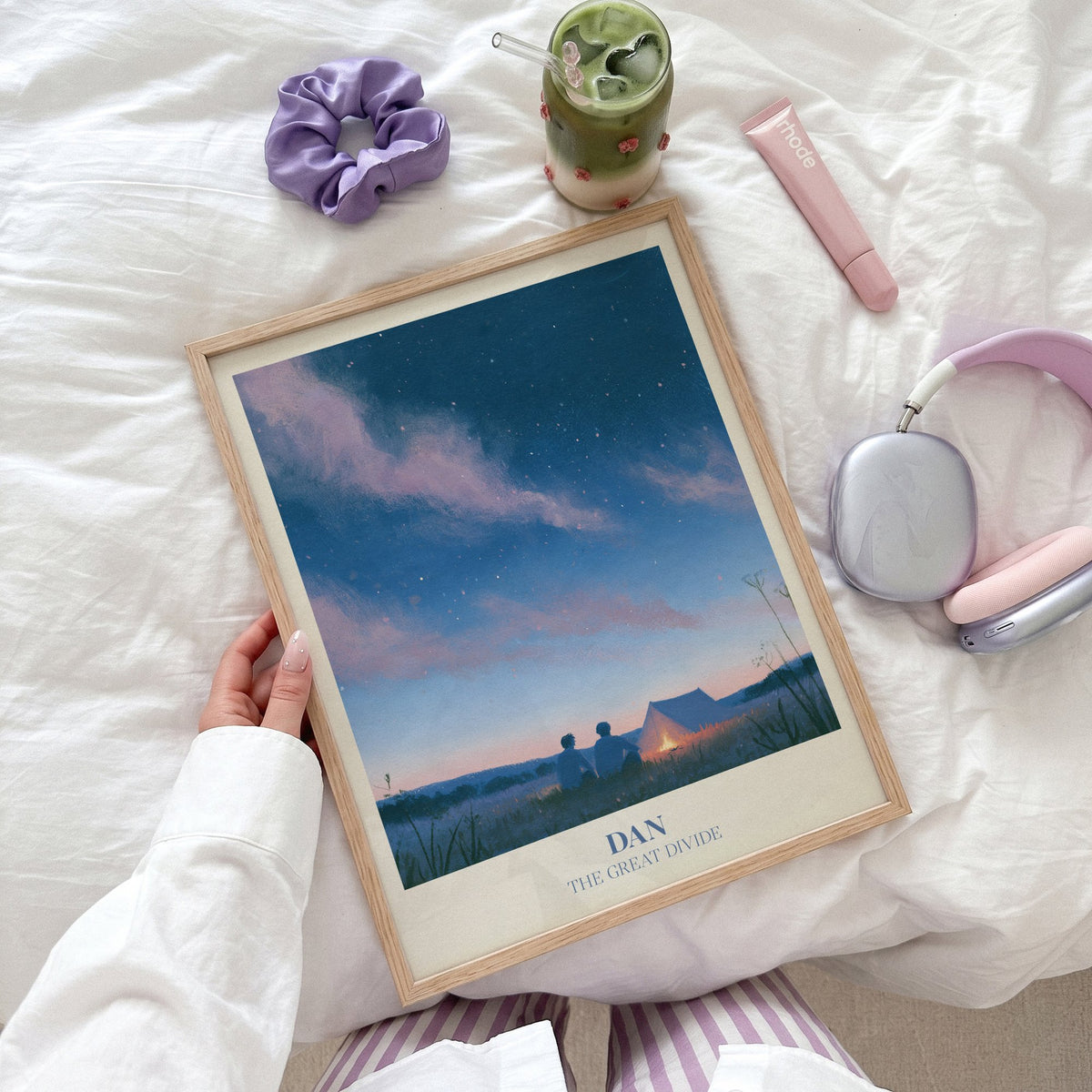 Dan Noah Kahan print of two friends by a campfire under the stars, held flat on a bed beside headphones and a scrunchie