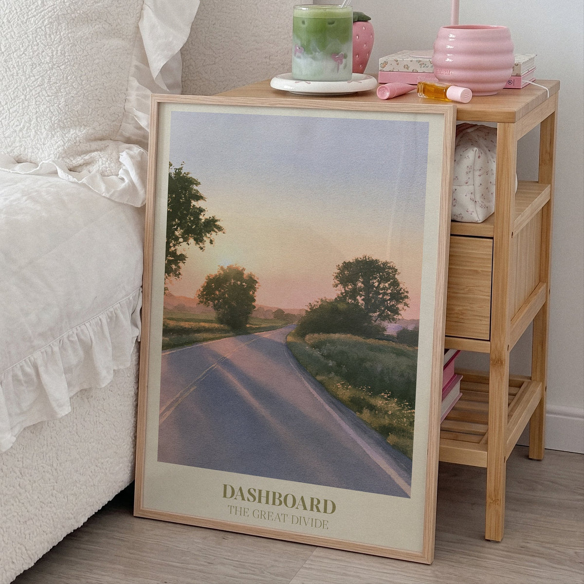 Dashboard Noah Kahan print of an empty country road at sunset, framed, leaning by a bed and a bamboo nightstand