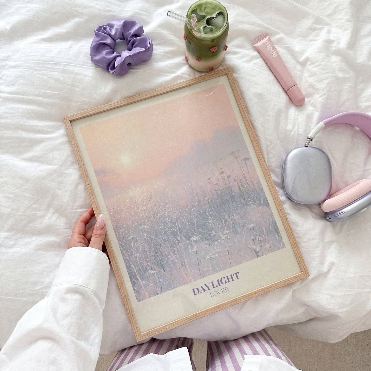 Daylight Winter Taylor Swift print of a frosty meadow at sunrise, held flat on a bed beside headphones and a scrunchie