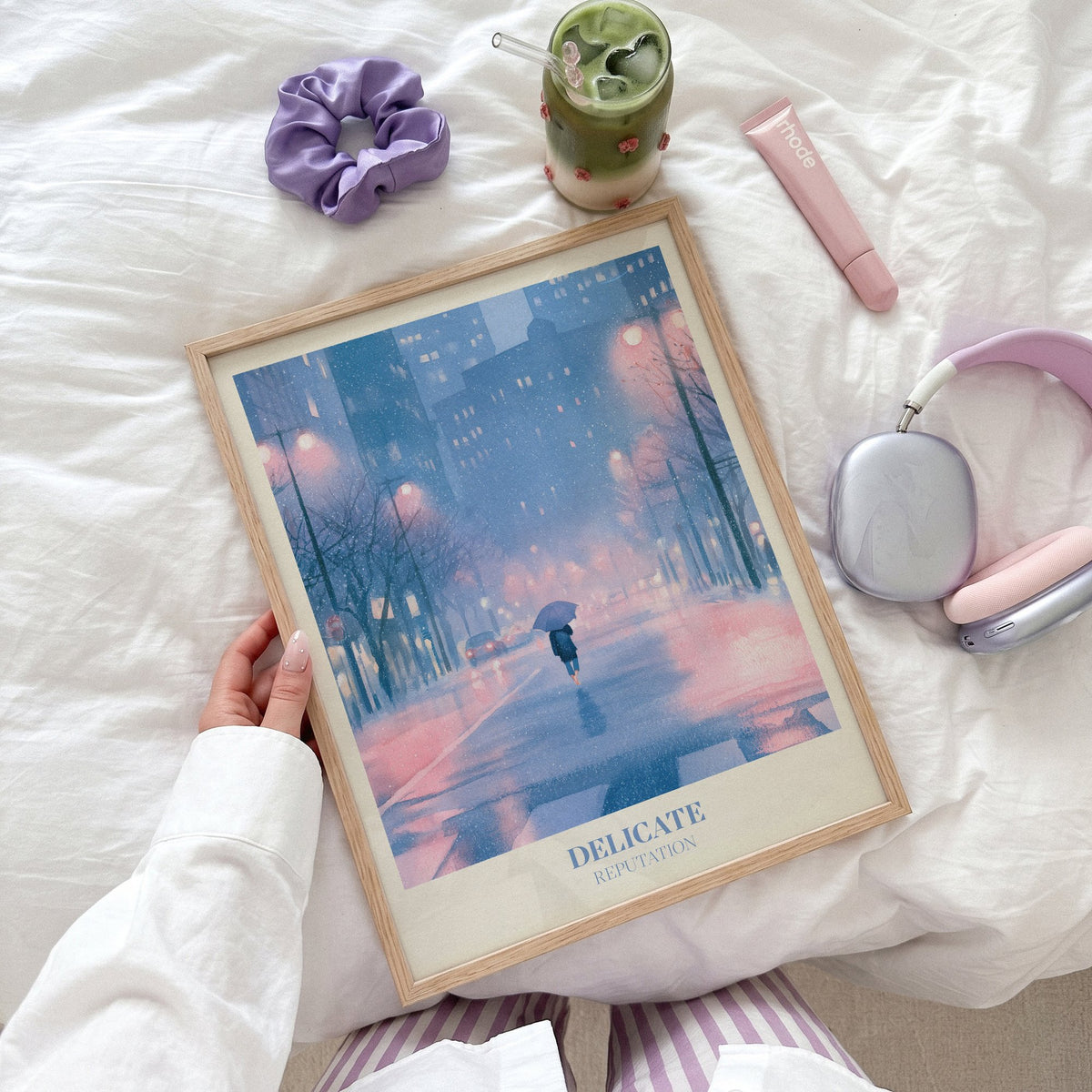 Delicate Taylor Swift print of a rainy city street at night, held flat on a bed beside headphones and a scrunchie