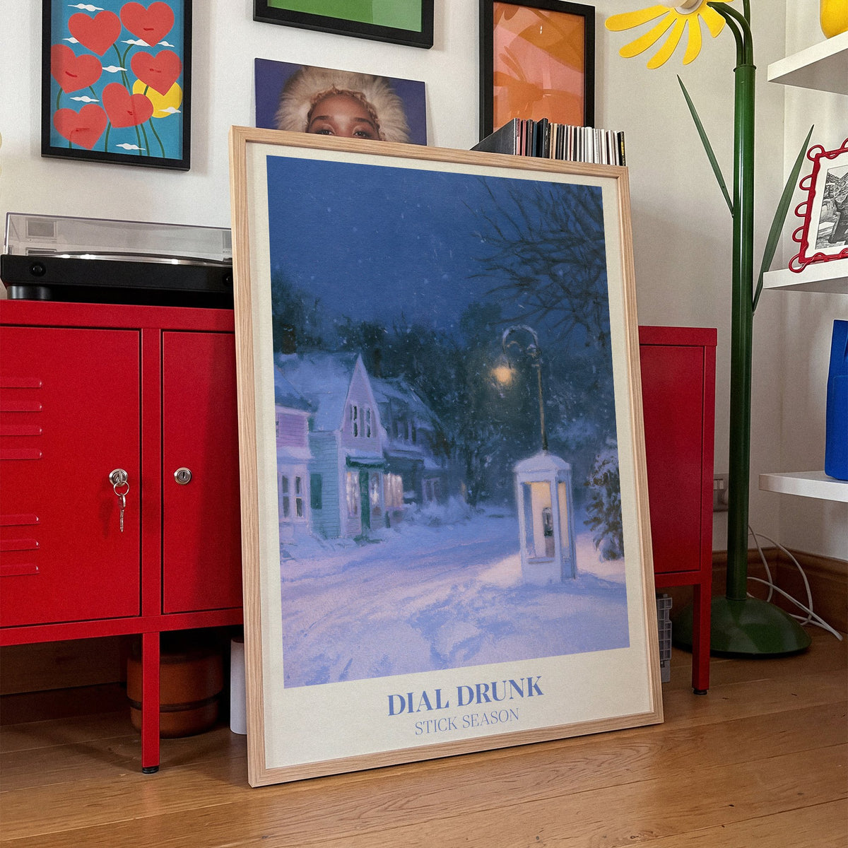 Dial Drunk Noah Kahan print of a phone box on a snowy village street at night, leaning against red lockers in a colourful living room