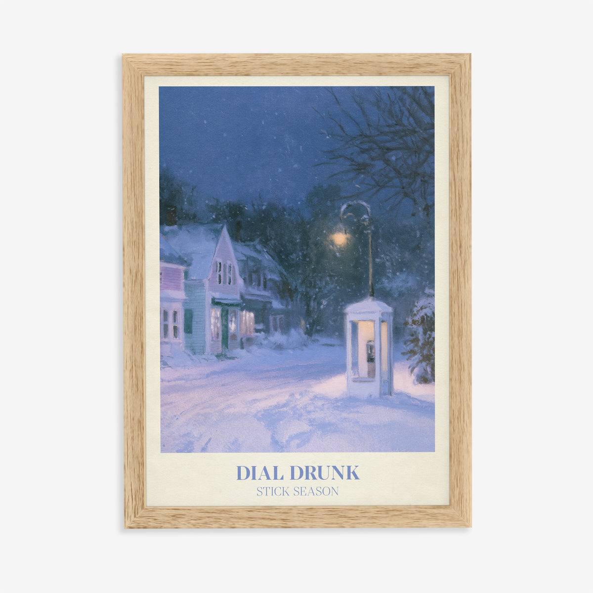 Dial Drunk Noah Kahan print of a phone box on a snowy village street at night, in an oak frame on a plain wall