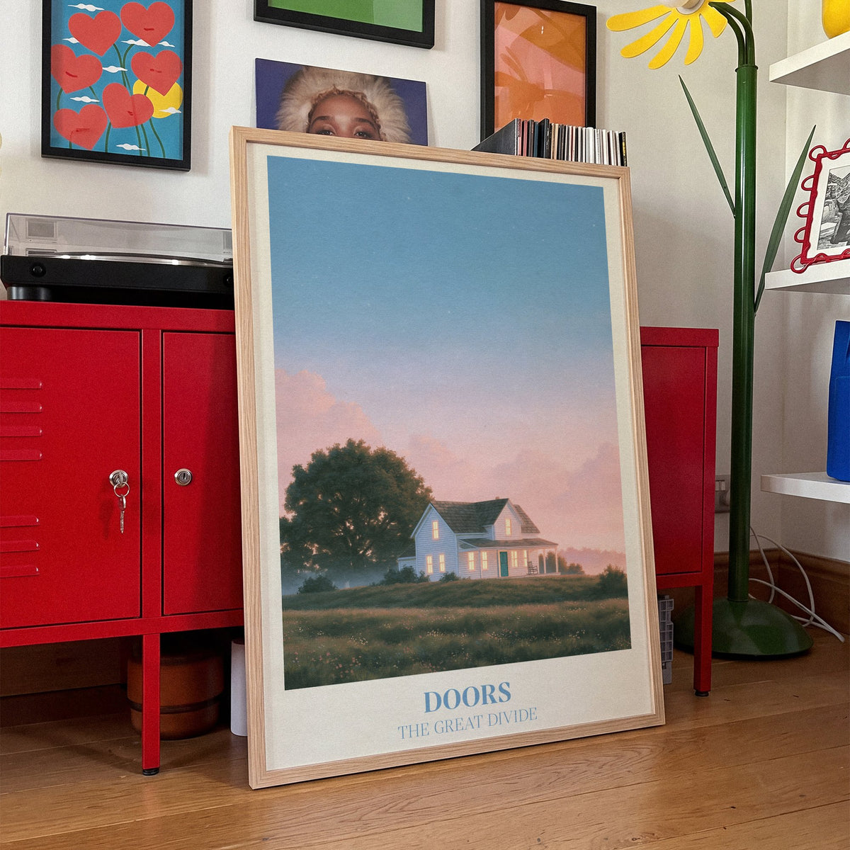 Doors Noah Kahan print of a white farmhouse glowing at dusk, framed, leaning against red lockers