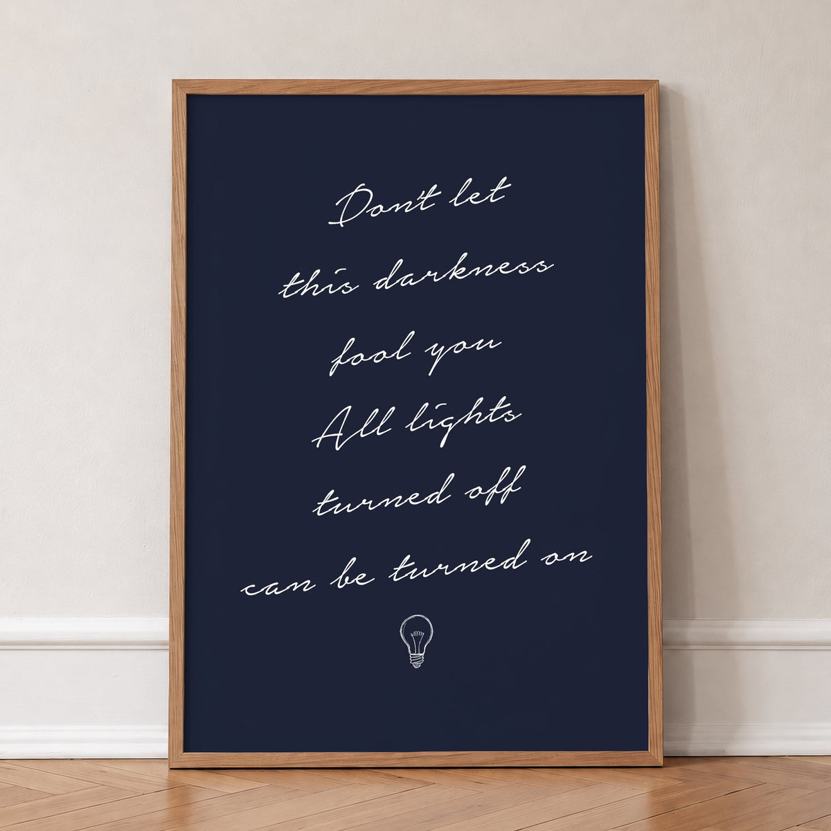 Don't Let This Darkness Fool You Noah Kahan lyric print in white handwriting on navy, in an oak frame, leaning against a wall on a herringbone floor
