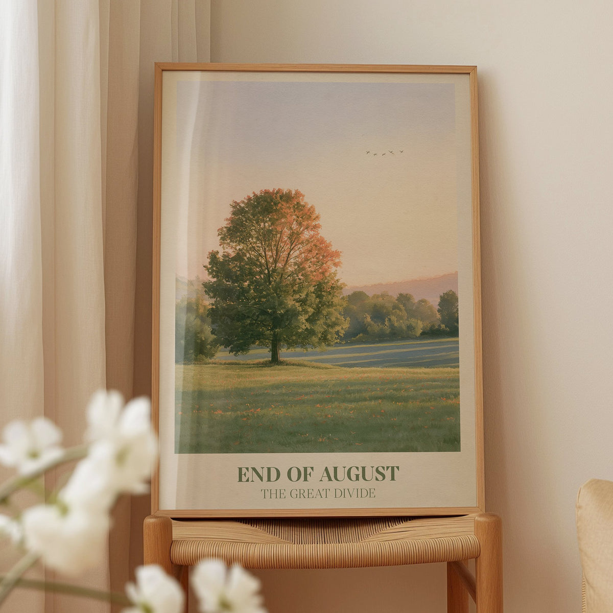 End of August Noah Kahan print of a lone tree in a late-summer field, framed on a wooden chair beside white blossom