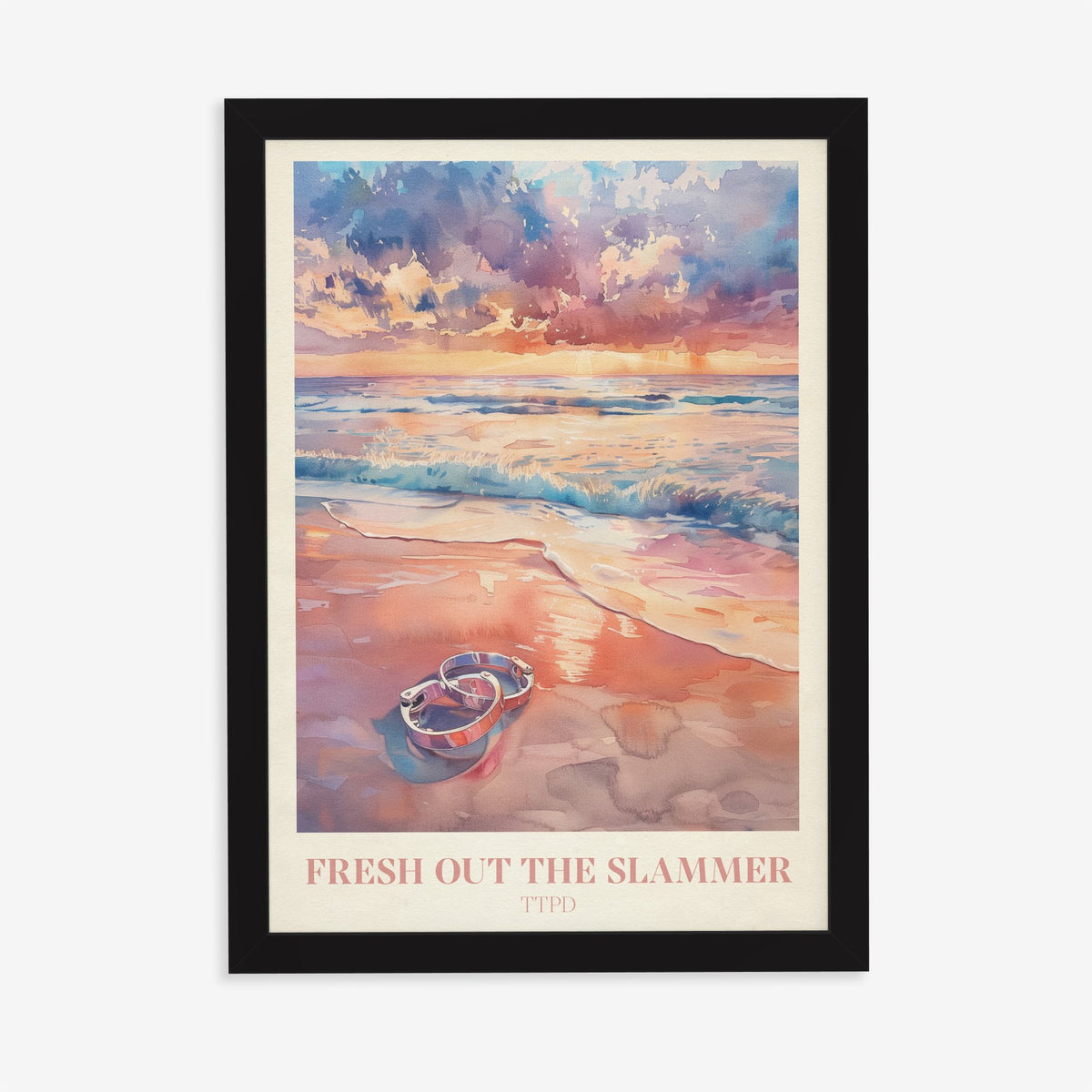 Fresh Out The Slammer Taylor Swift print of open handcuffs on wet sand at a pink sunset, in a black frame on a plain wall