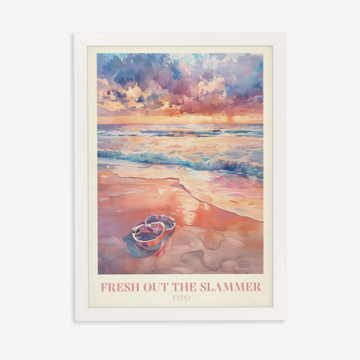 Fresh Out The Slammer Taylor Swift print of open handcuffs on wet sand at a pink sunset, in a white frame on a plain wall