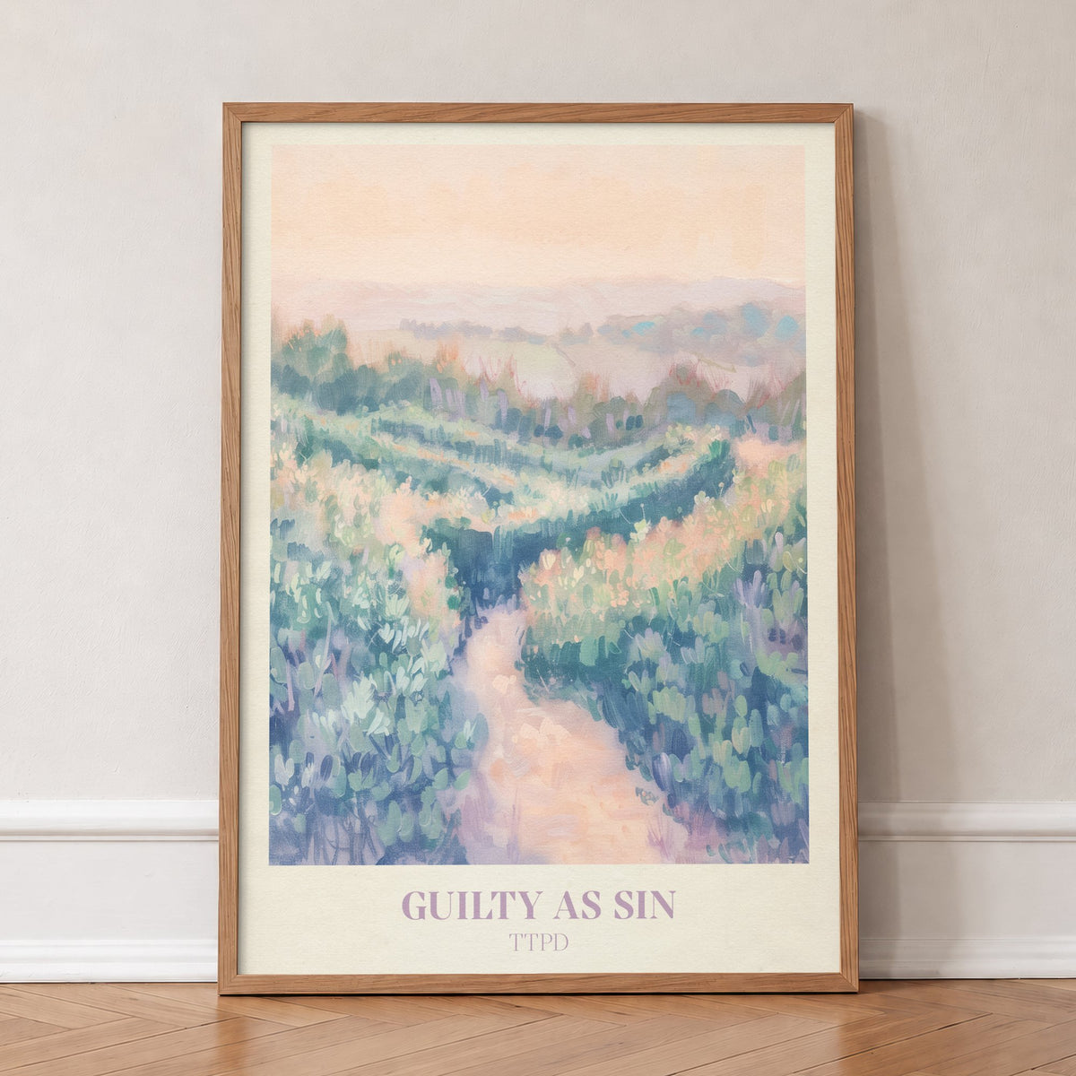 Guilty As Sin Taylor Swift print of a winding path through pastel green hills under a peach sky, in an oak frame, leaning against a wall on a herringbone floor