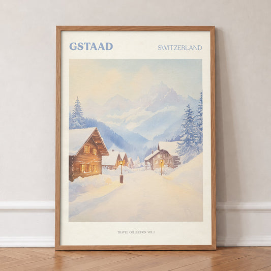 Gstaad travel print of snow-covered wooden chalets and pine trees below the Swiss Alps, in an oak frame, leaning against a wall on a herringbone floor
