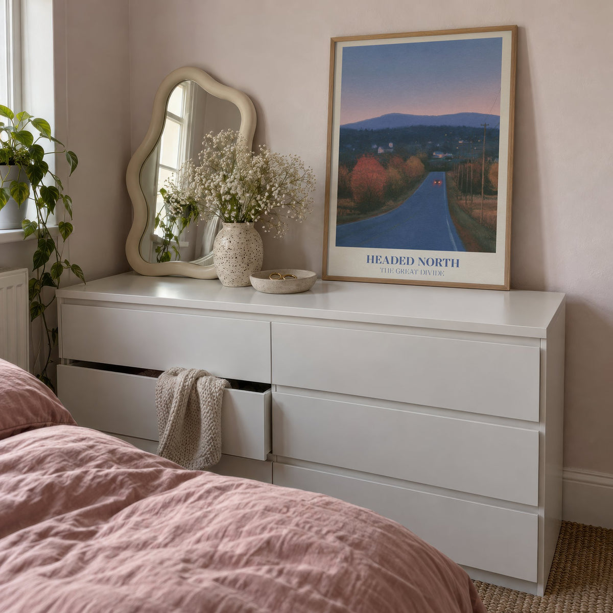 Headed North Noah Kahan print of a country road through autumn trees at dusk, framed, leaning on a white dresser beside a wavy mirror