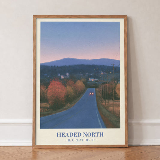 Headed North Noah Kahan print of a country road through autumn trees at dusk, in an oak frame, leaning against a wall on a herringbone floor