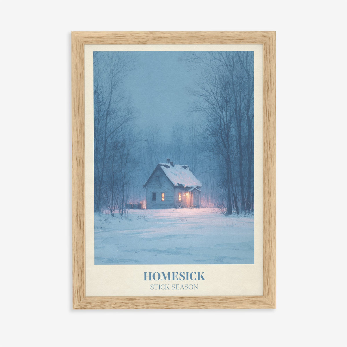 Homesick Noah Kahan print of a snowy cabin with glowing windows in a winter forest, in an oak frame on a plain wall