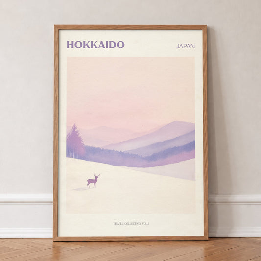 Hokkaido travel print of a lone deer in deep snow below soft pink and lilac hills, in an oak frame, leaning against a wall on a herringbone floor