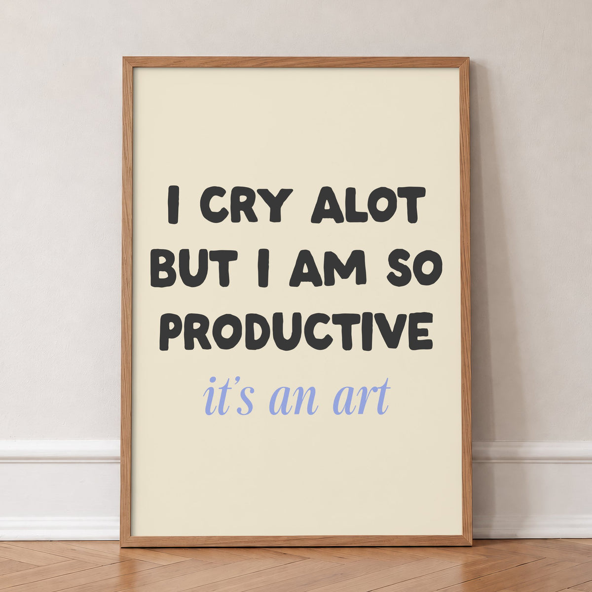 I Cry A Lot But I’m So Productive Taylor Swift lyric print of black and blue lettering on cream, in an oak frame, leaning against a wall on a herringbone floor