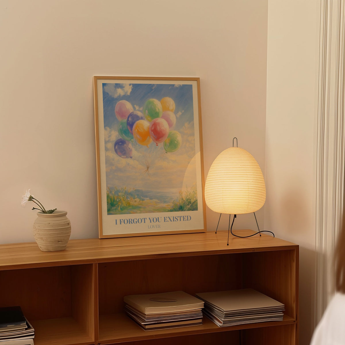 I Forgot You Existed Taylor Swift print of pastel balloons floating over the sea, framed on a shelf beside a paper lantern