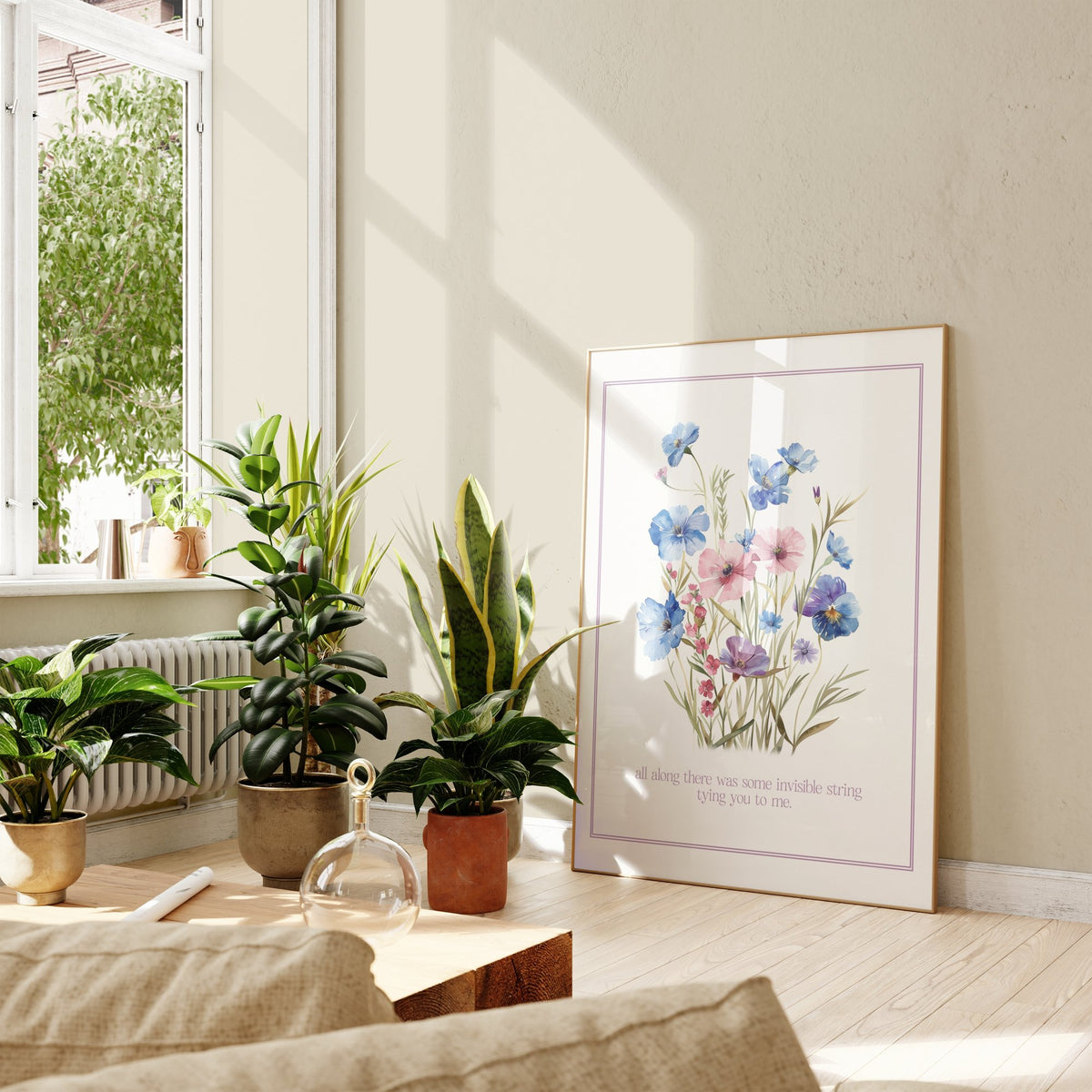 Invisible String Botanical Taylor Swift print of blue and pink wildflowers, framed, leaning against a wall beside potted plants