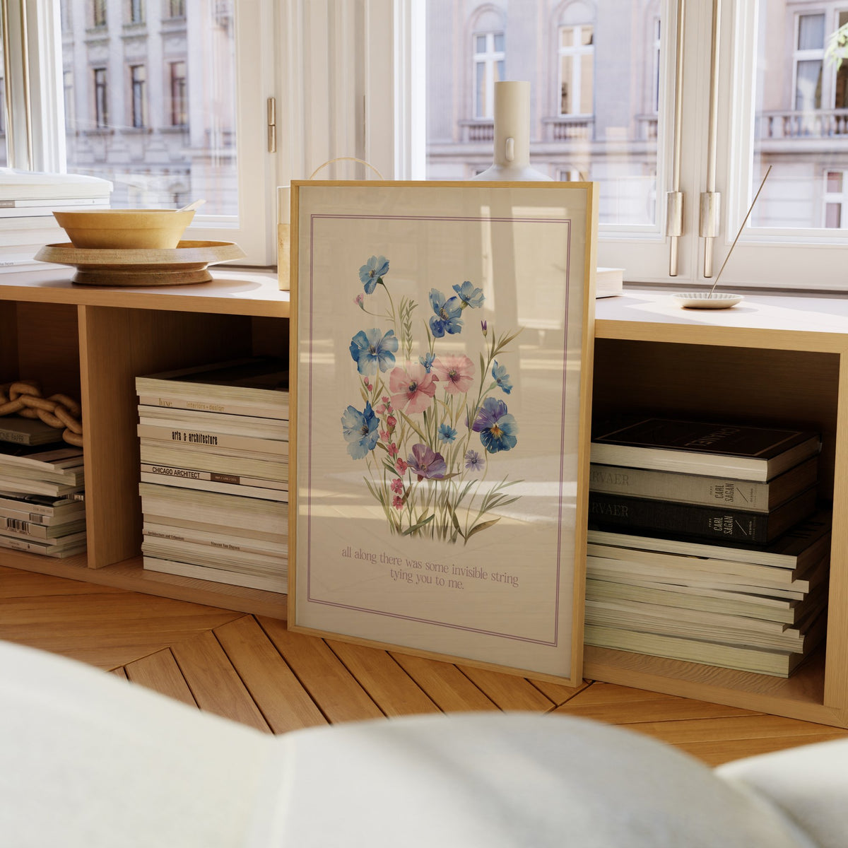 Invisible String Botanical Taylor Swift print of blue and pink wildflowers, framed on a bookcase by a window