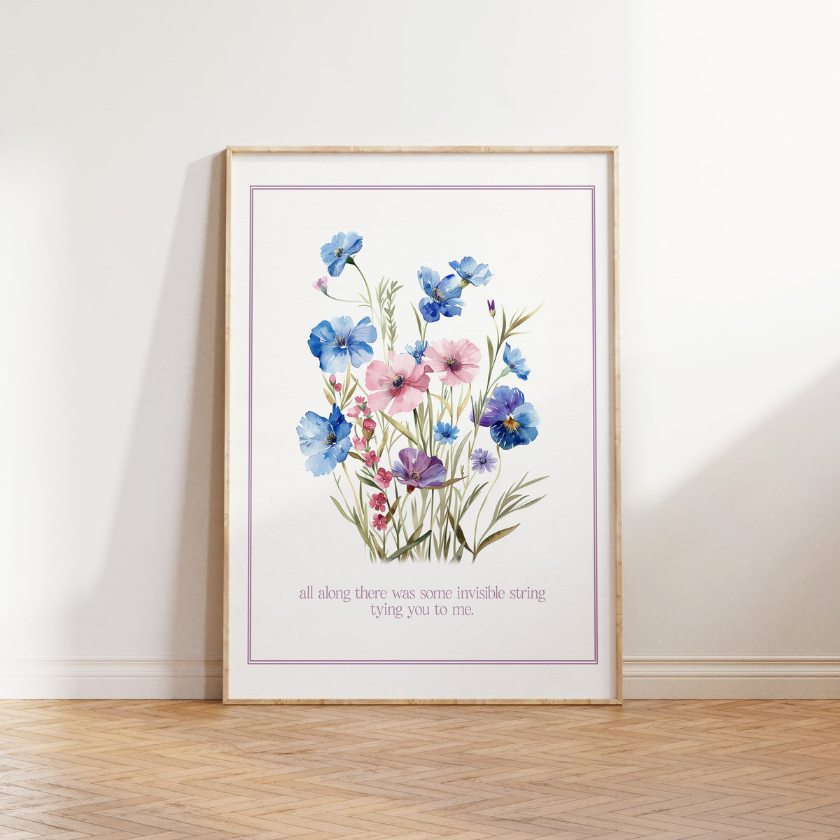 Invisible String Botanical Taylor Swift print of blue and pink wildflowers, framed, leaning against a white wall