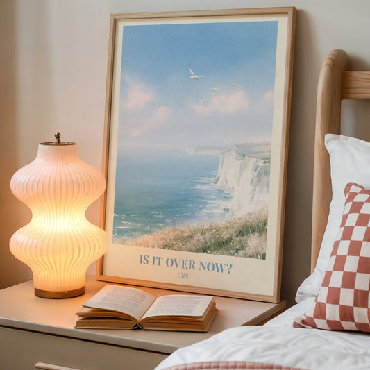 Is It Over Now? Taylor Swift print of white cliffs above a blue sea, on a bedside table next to a lamp